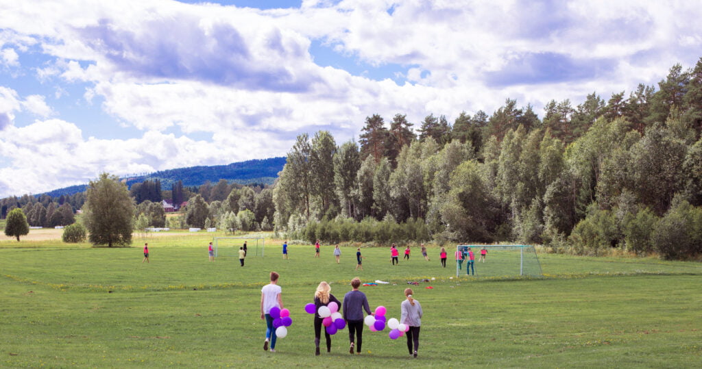 Ungdomar går över fält med ballonger